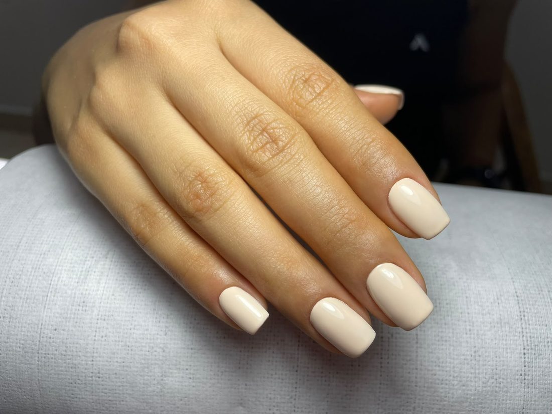 Mano con uñas cuadradas cortas en tono crema brillante