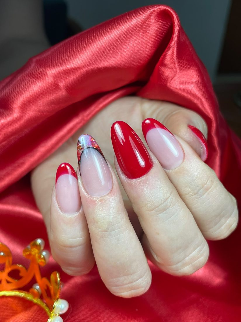 Uñas almendradas en rojo con francesa roja y un acento de brillos, sobre satín rojo